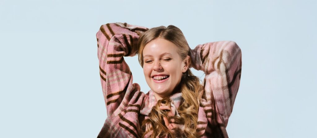 A white girl in Pink plaid leaning back and laughing in front of a blue background.