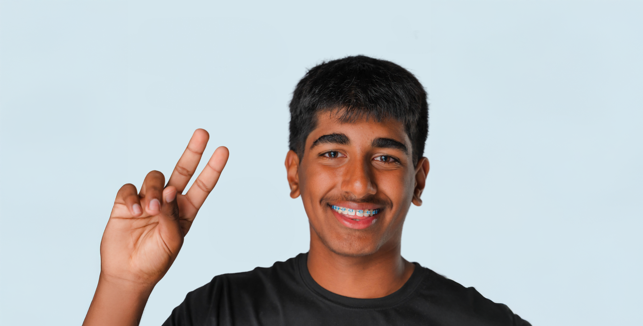 A happy latin boy with lightforce braces giving the peace sign with his right hand.