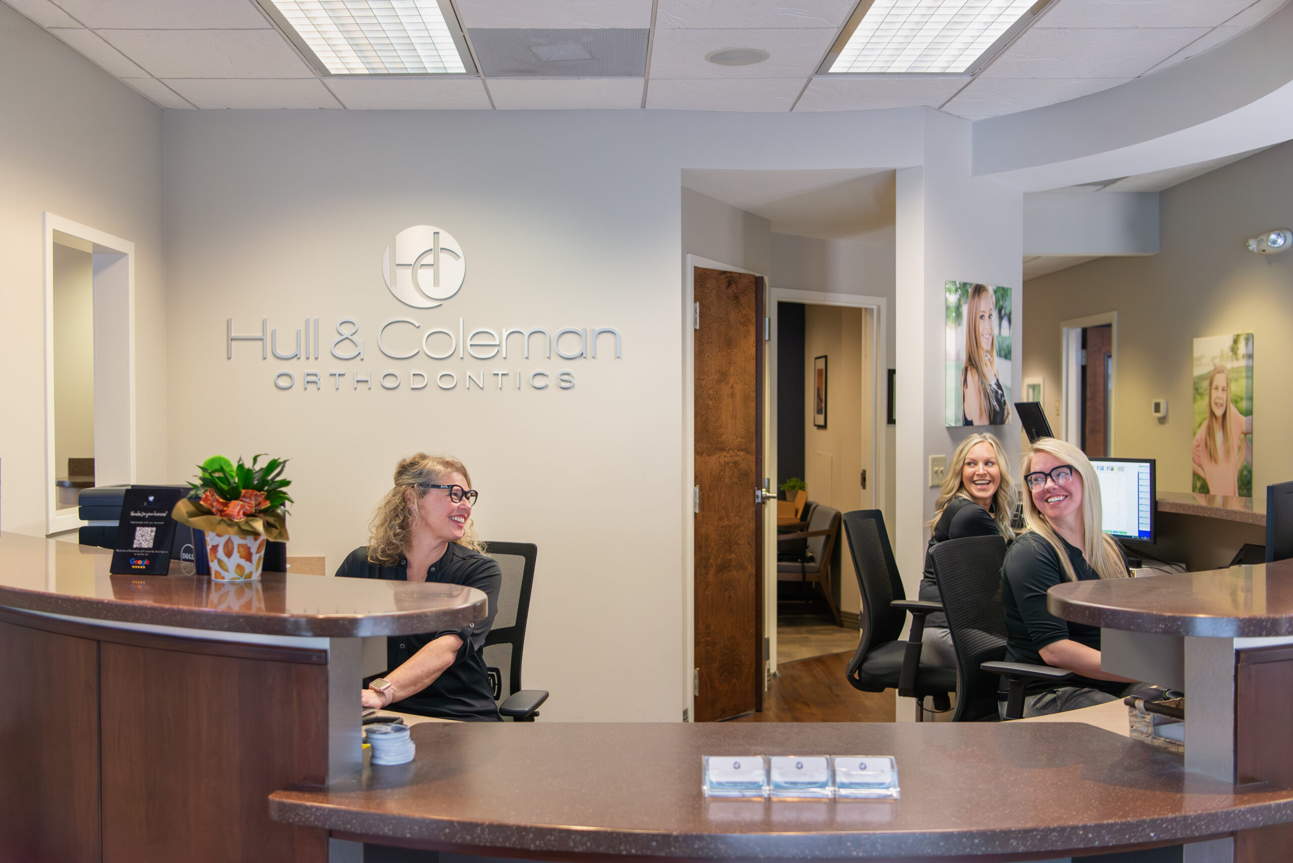 Female receptionists at an orthodontic office front desk smile and talk to each other.